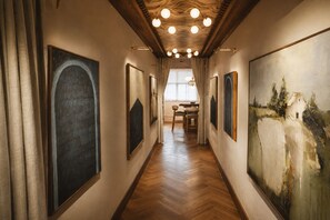 A hallway with wooden flooring, framed artworks on the walls, and a dining area in the background.
