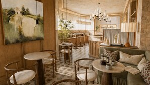 Un intérieur chaleureux avec des tables rondes, des chaises en bois, un canapé et un tableau accroché au mur.