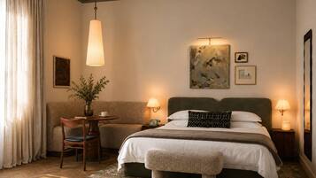 A hotel room with a bed, bedside tables, a desk with a chair, a vase with flowers, and artwork on the wall.