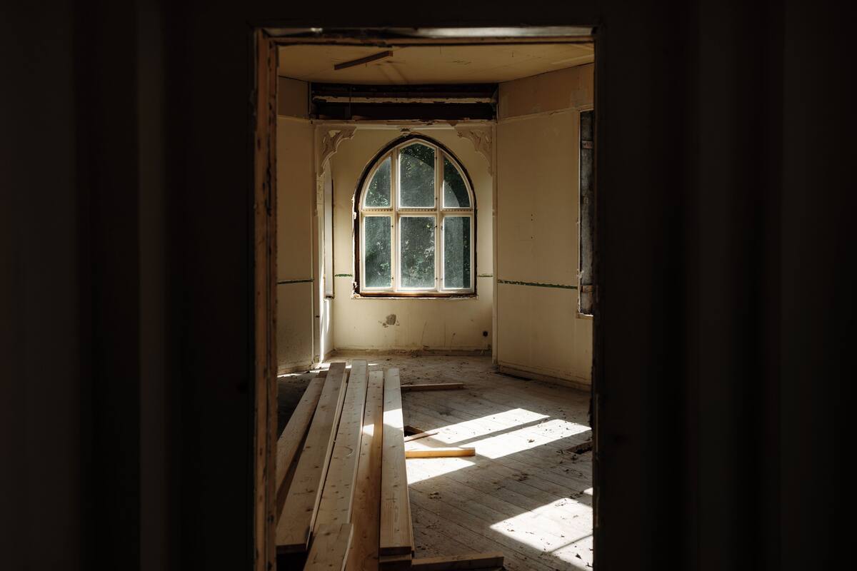 An interior space with a large arched window, wooden flooring, and a door leading outside.