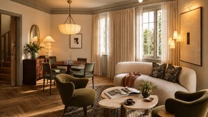 Un salon bien éclairé, avec un canapé, des fauteuils, une table à manger et un lustre.