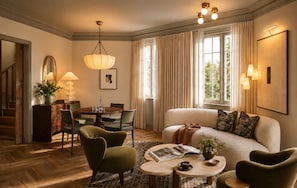 Ein helles Wohnzimmer mit einer Couch, Stühlen, einem Esstisch und einer Deckenleuchte.