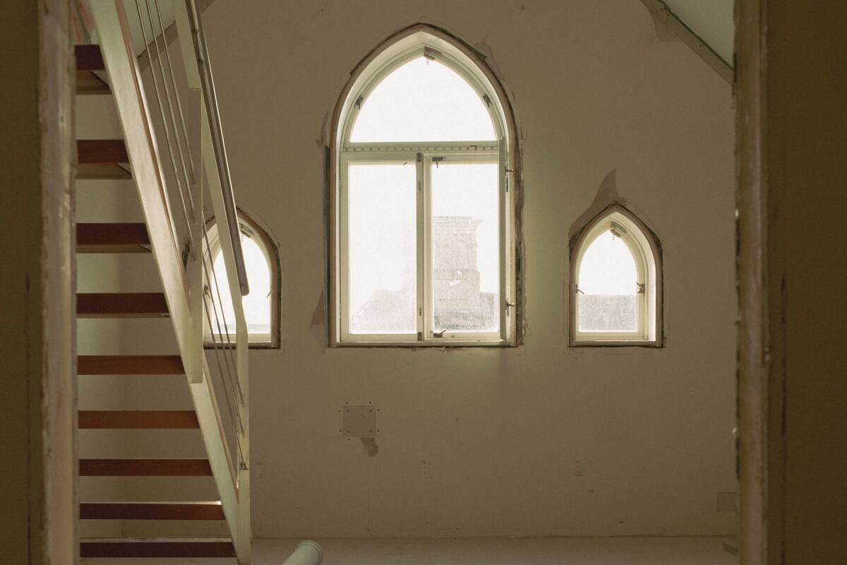 An attic room with a sloped ceiling, a large arched window, and a staircase.