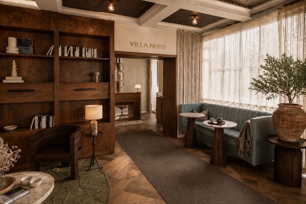 A cozy living area with a sofa, a fireplace, a bookshelf, and a large window with curtains.