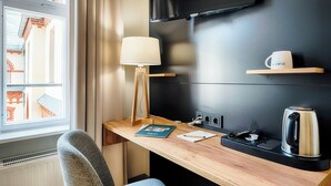 Une chambre d’hôtel avec un bureau en bois, une lampe, un téléviseur à écran plat fixé au mur, une bouilloire et une tasse à café posée sur une étagère.