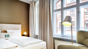 Une chambre d’hôtel avec un lit, une chaise, une lampe et une fenêtre avec des rideaux.