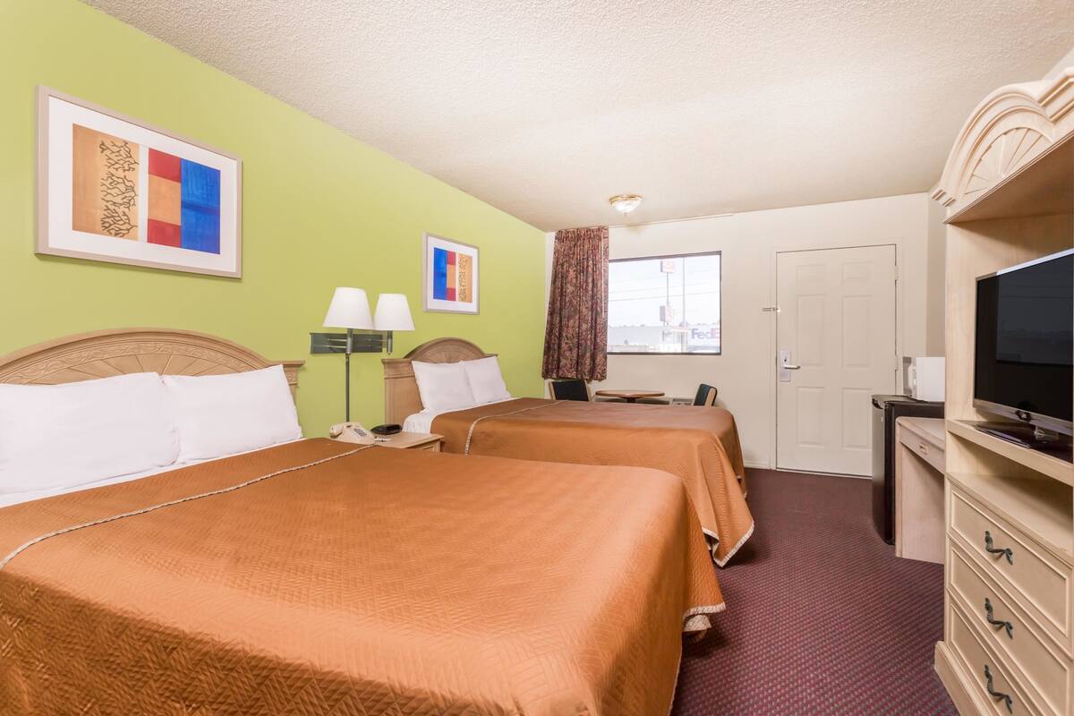 A hotel room with two beds, a television, a desk, and a window with a view of a building.