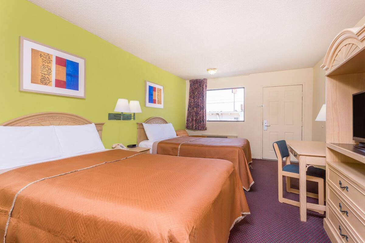 A hotel room with two beds, a desk, a chair, a television, and artwork on the walls.