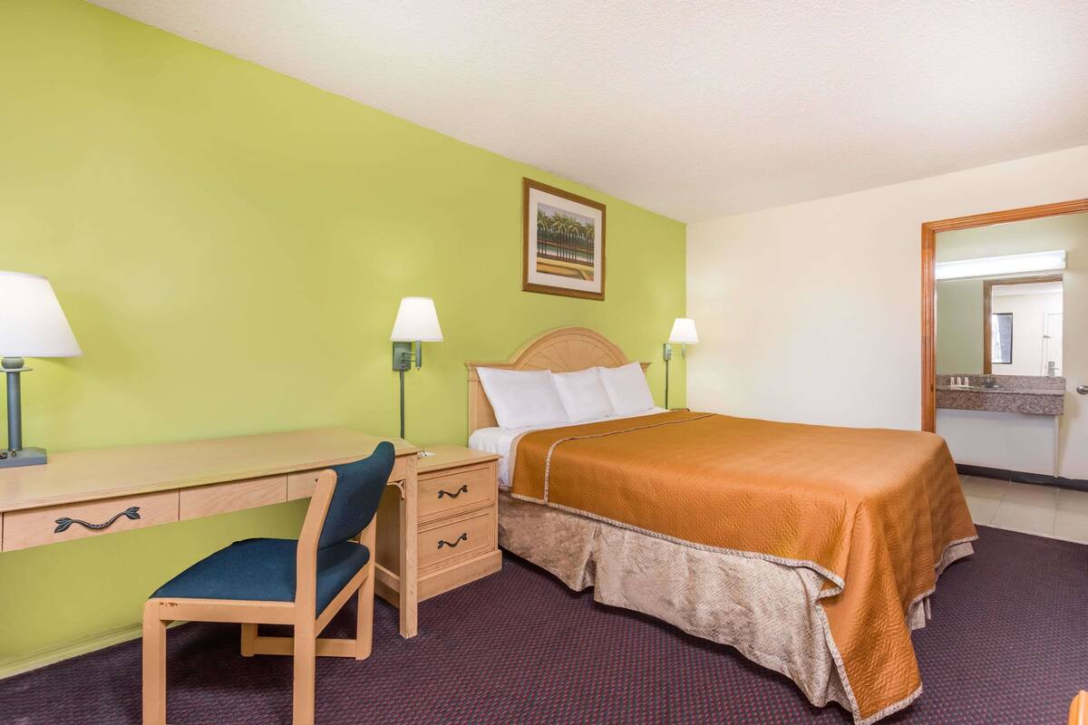 A hotel room with a bed, desk, chair, and two bedside lamps.