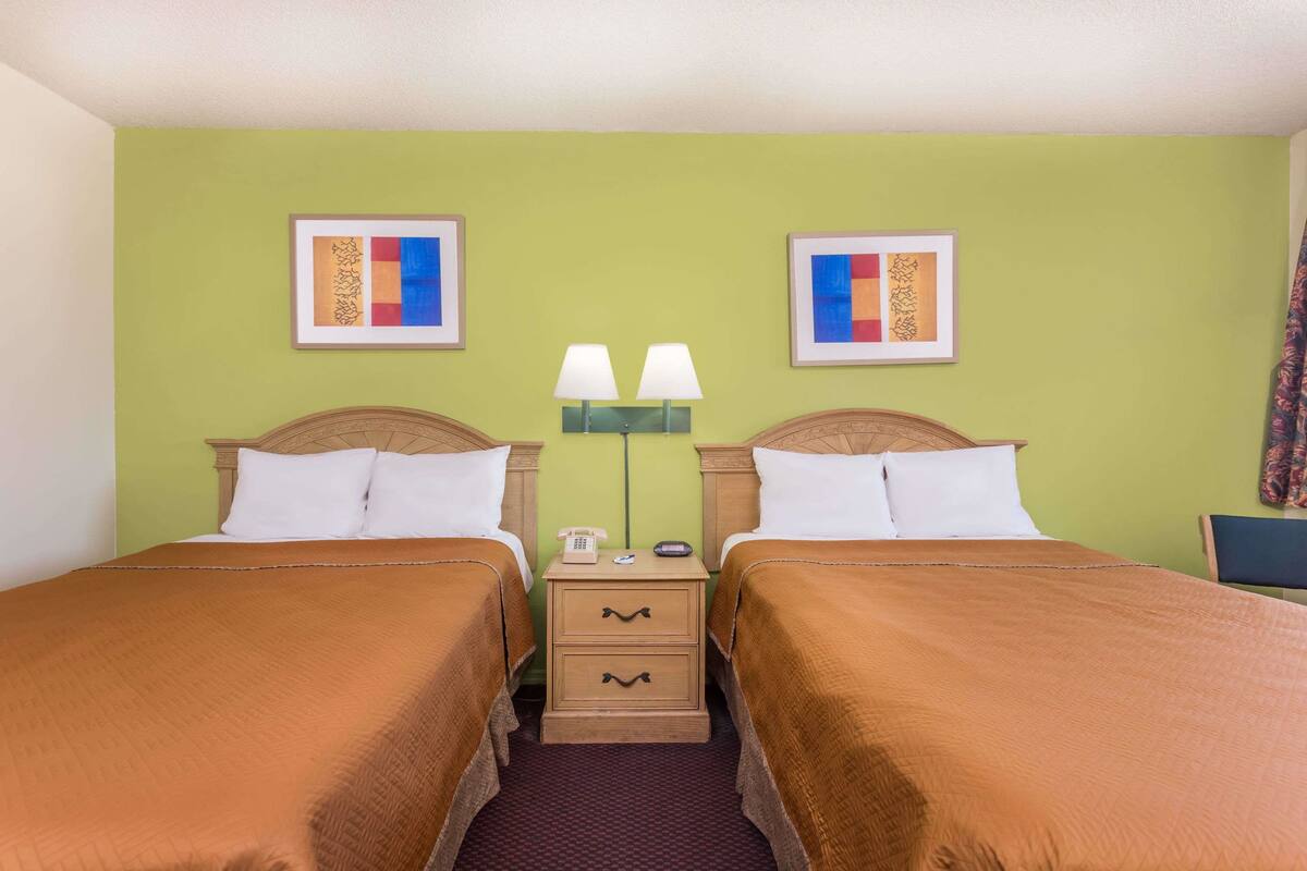 A hotel room with two beds, green walls, and artwork on the walls.