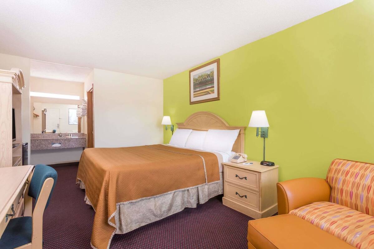 A hotel room with a bed, bedside table, lamp, chair, and a desk.