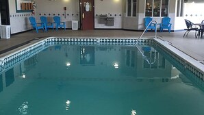 An indoor swimming pool with blue chairs around it, a ceiling fan, and a door in the background. - Osceola Grand Hotel (Evart)