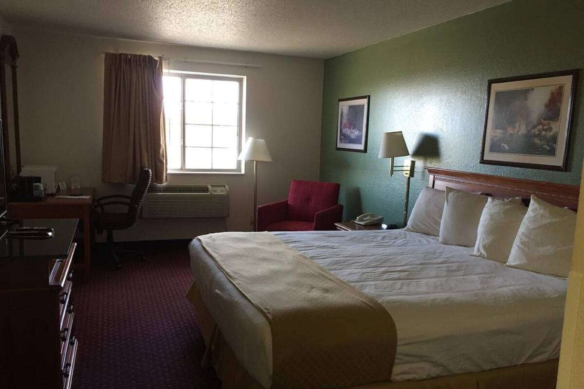 Ein Hotelzimmer mit einem großen Bett, einem Schreibtisch, einem Stuhl und einem fenster mit Vorhängen.