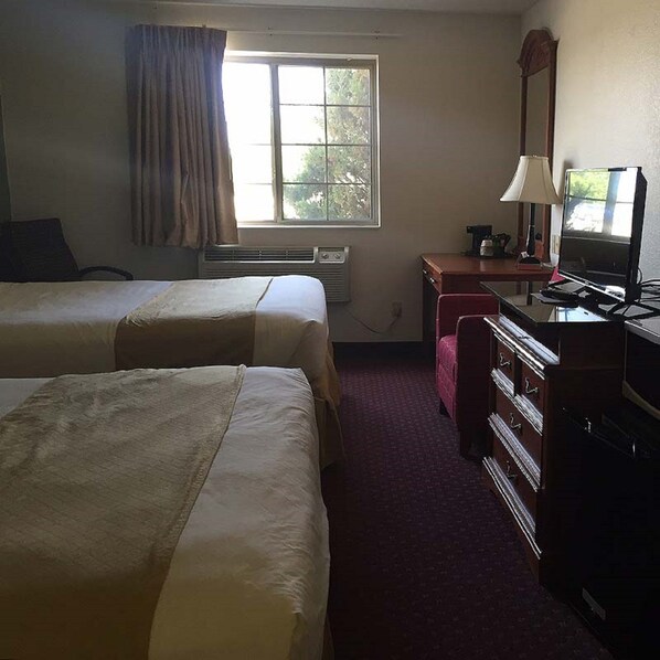 A hotel room with two beds, a desk with a computer, a lamp, and a window with curtains.