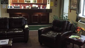 A lobby with leather sofas, a reception desk, and a small table with magazines. - Osceola Grand Hotel (Evart)