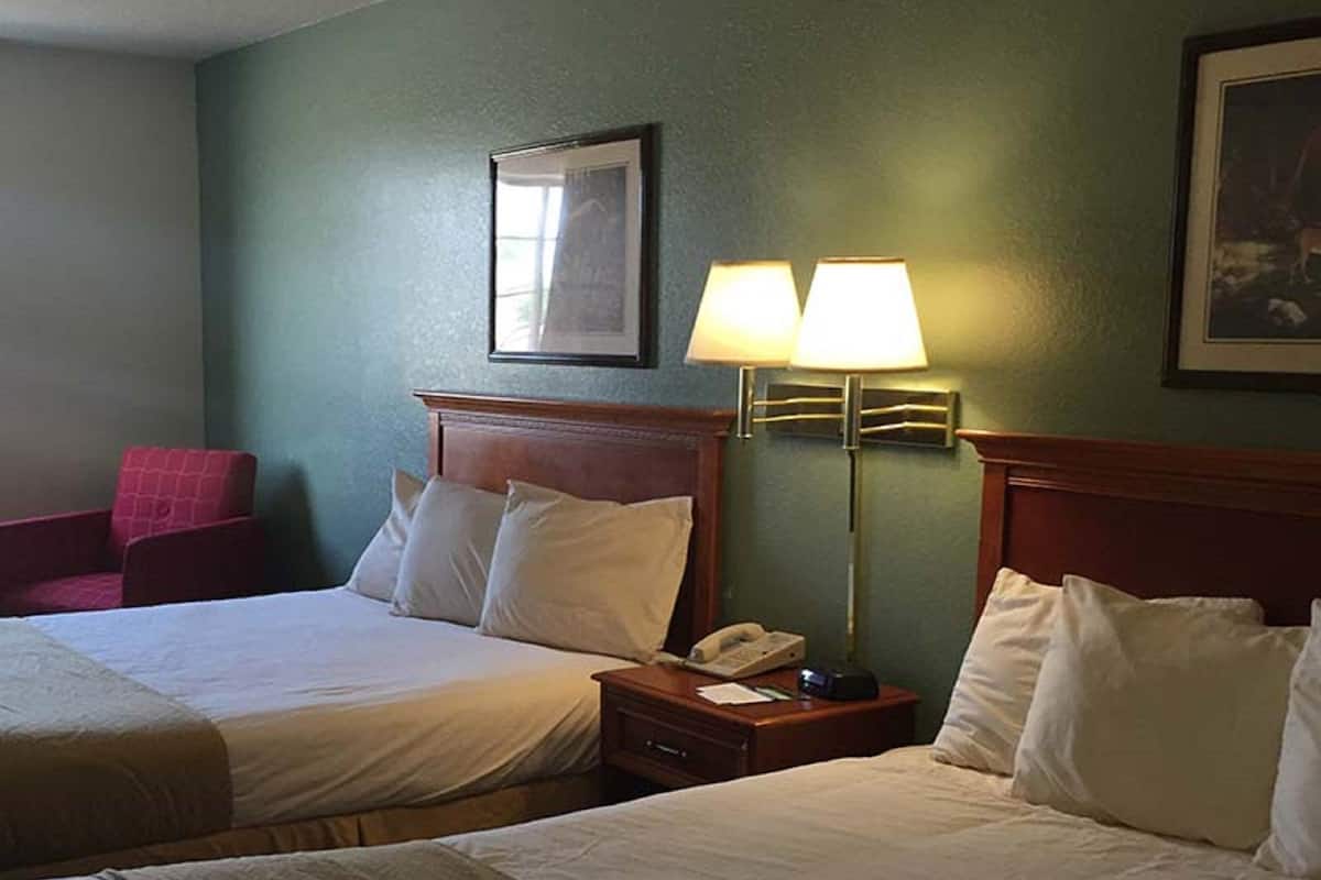 Ein Hotelzimmer mit zwei Betten, einem roten Sessel, einer Lampe und einem gerahmten Bild an der Wand.
