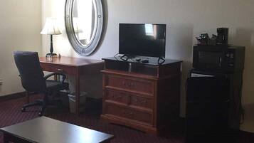 Une chambre d’hôtel équipée d’un bureau, d’une chaise, d’une télévision, d’une commode et d’un four à micro-ondes.