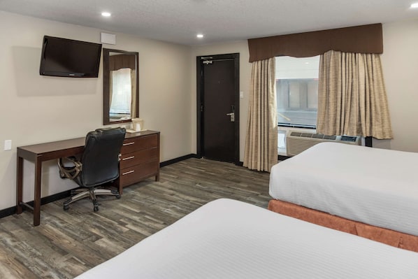 Ein Hotelzimmer mit einem Bett, einem Schreibtisch, einem Stuhl, einem Fernseher und einer Tür.