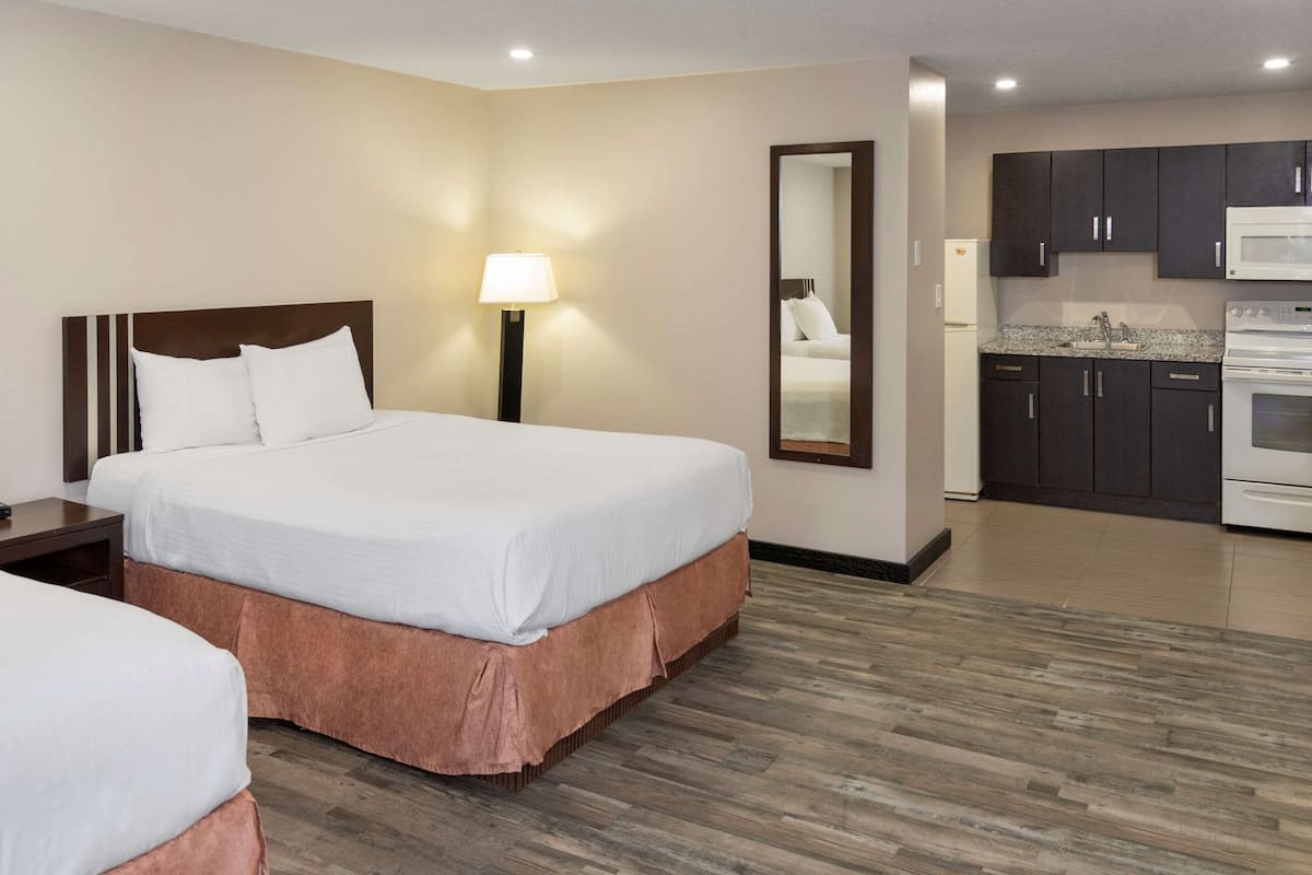 A hotel room with a double bed, bedside tables, a lamp, a mirror, a kitchenette with a microwave, and a wooden floor.