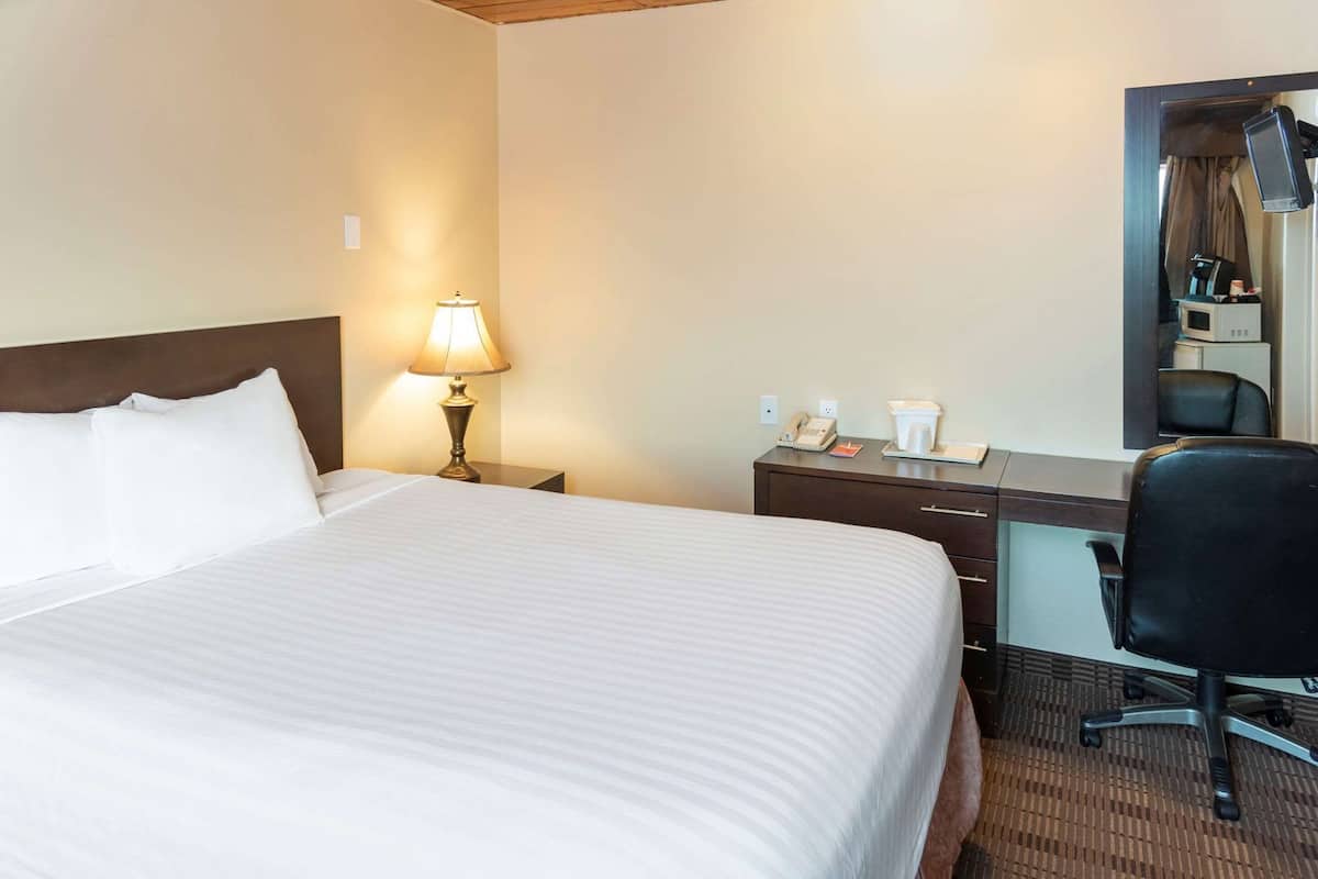 A hotel room with a large bed, a desk with a chair, a lamp, a telephone, and a coffee maker.