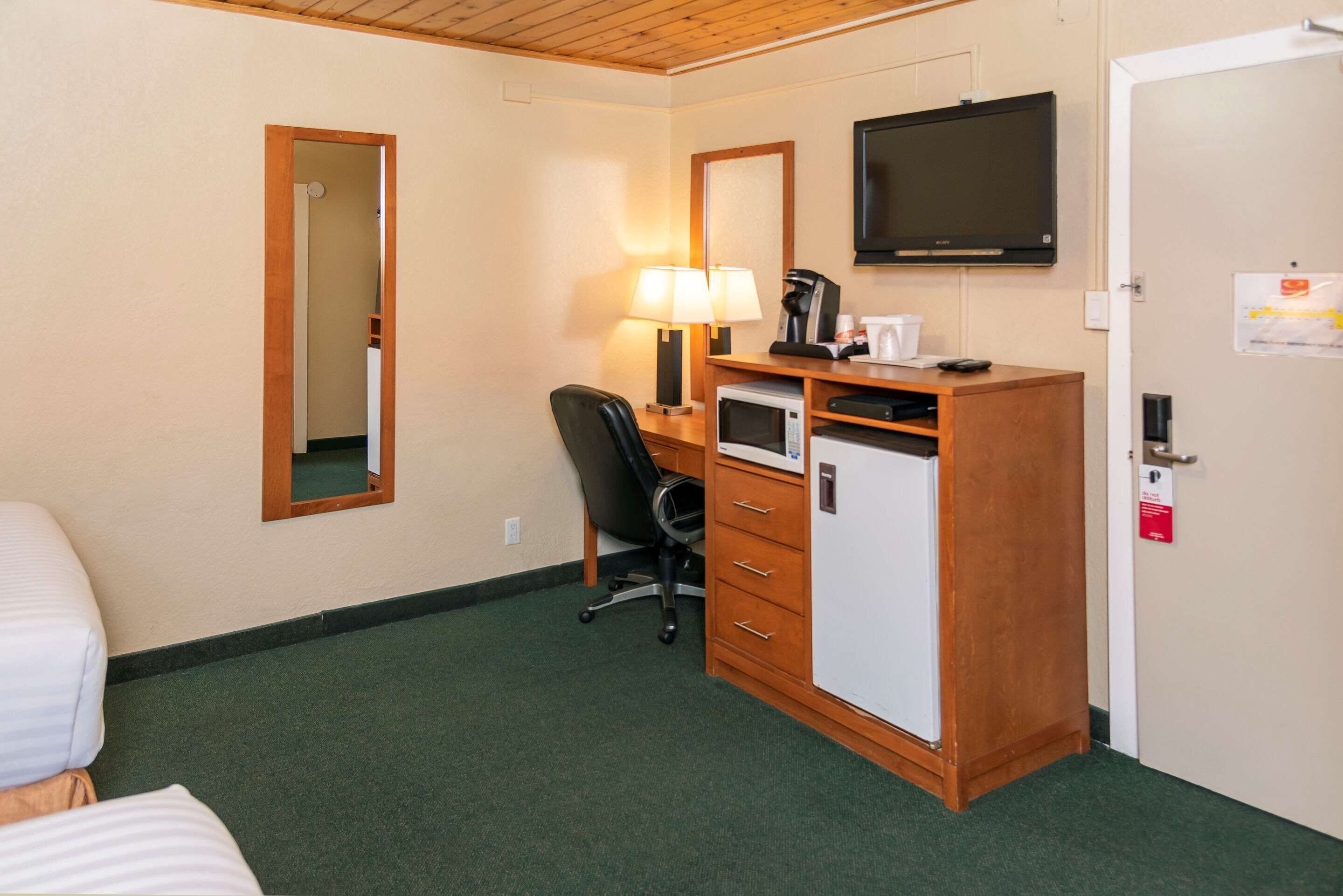 A hotel room with a bed, a desk with a computer, a chair, a television, and a microwave.
