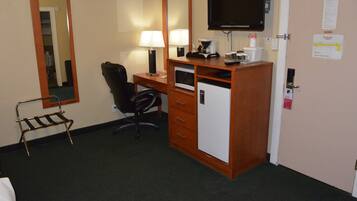 A hotel room with a desk, chair, small refrigerator, and a television mounted on the wall.