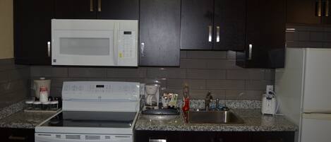 A kitchen with dark cabinets, a white microwave, a stove, and a sink.
