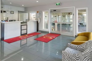 Ein Hotel-Empfangsbereich mit einer Rezeption, einem roten Teppich, einem gelben Sofa und einem Couch mit Zepramuster.
