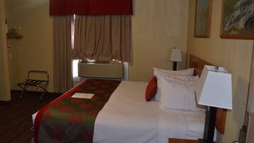 Hotelkamer met een bed, een bedlamp, een raam met gordijnen, een radiator en een aan de muur hangend schilderij.