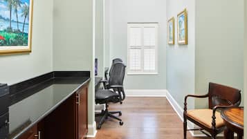 Un couloir avec un plancher en bois, une chaise de bureau noire, une table à manger en bois et un tableau encadré accroché au mur.