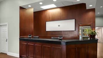 A reception desk with a flat-screen TV, wooden paneling, and a potted plant.