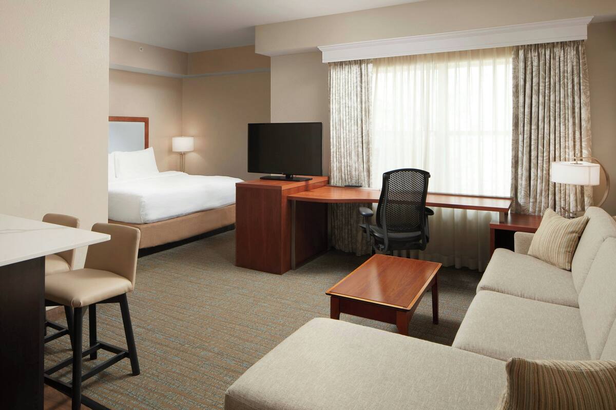 A hotel room with a bed, a desk with a computer, a TV, a sofa, and a chair.