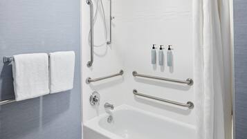 Ein modernes Badezimmer mit Badewanne, Haltegriffen, einem Handtuchhalter und Toilettenartikeln.