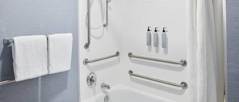 A modern bathroom with a bathtub, grab bars, a towel rack, and toiletries.