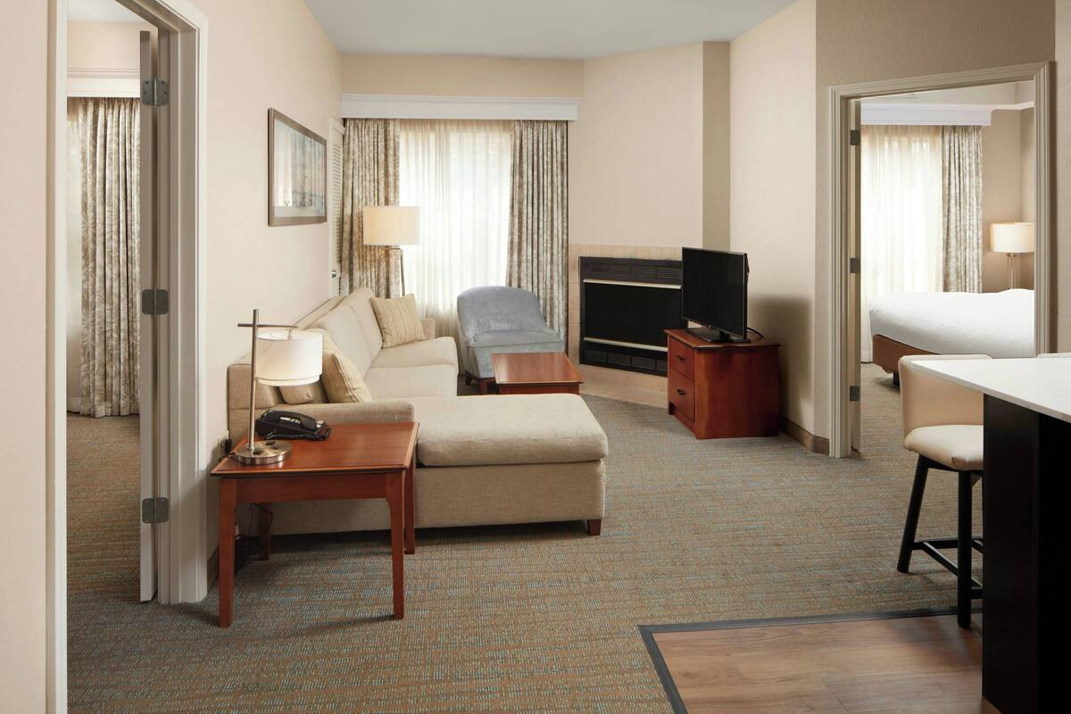 A hotel room with a bed, a sofa, a desk, a chair, a TV, and a lamp.