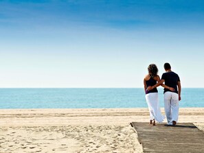 A couple standing on a wooden deck at a beach with a clear sky. - ibis Barcelona Castelldefels (Castelldefels)