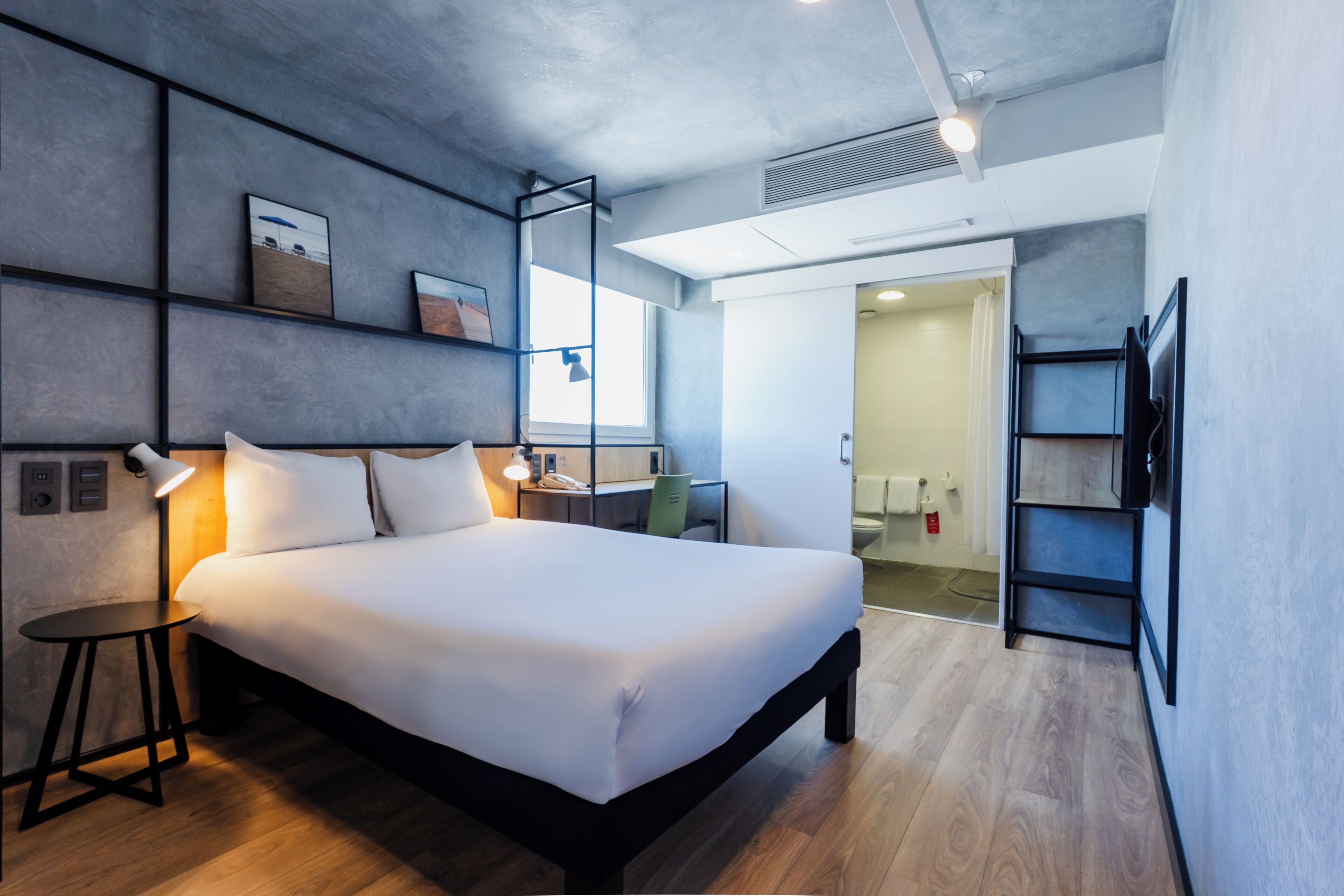 Ein modernes Hotelzimmer mit einem großen Bett, Nachttisch, Lampe und einem Schreibtisch mit Stuhl.