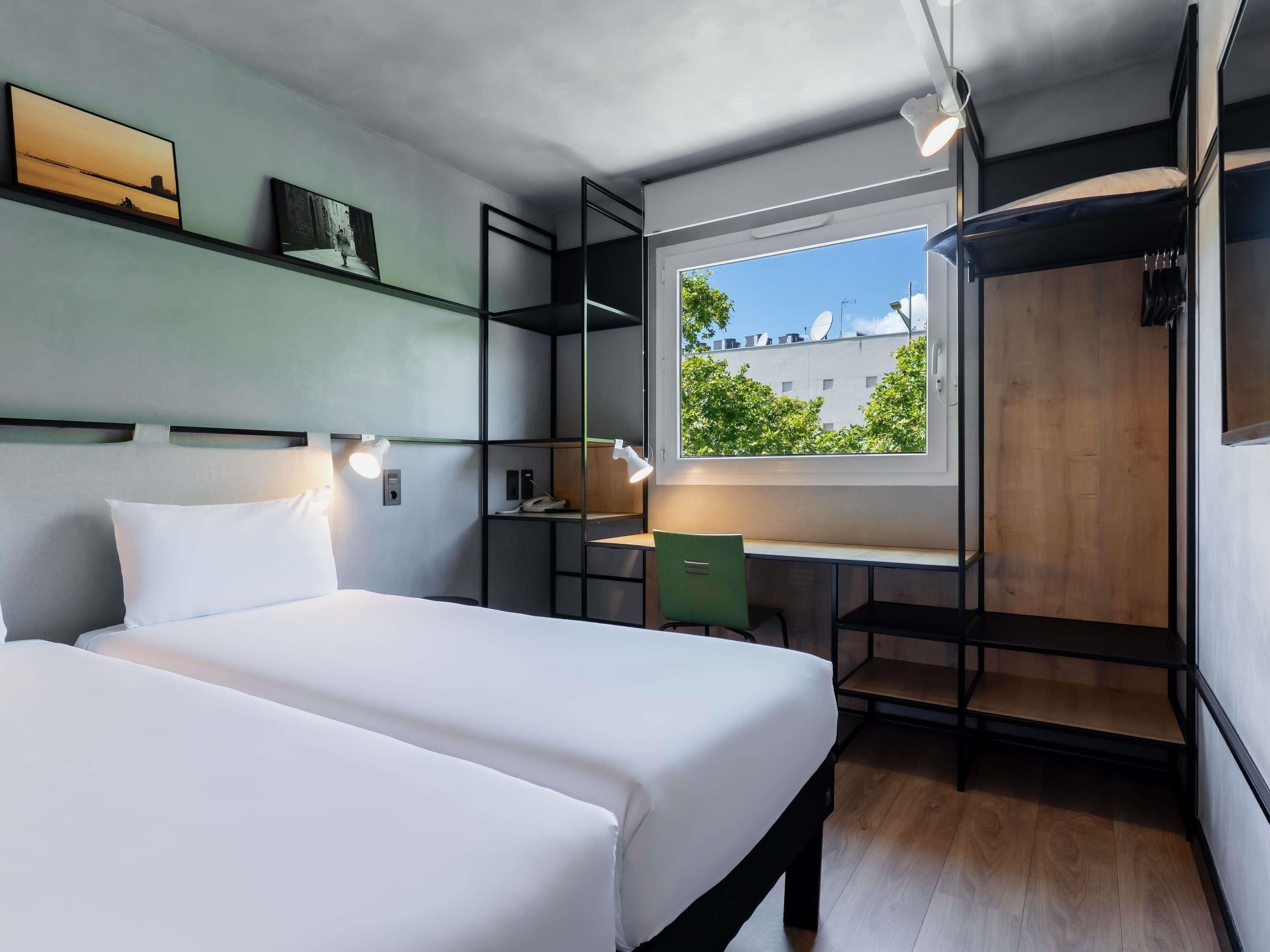Una habitación moderna con dos camas, un escritorio y una ventana que da a edificios.