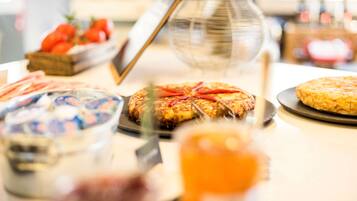 A buffet table with various dishes, including a pie with red peppers, a bowl of fruit, and a glass of orange juice.