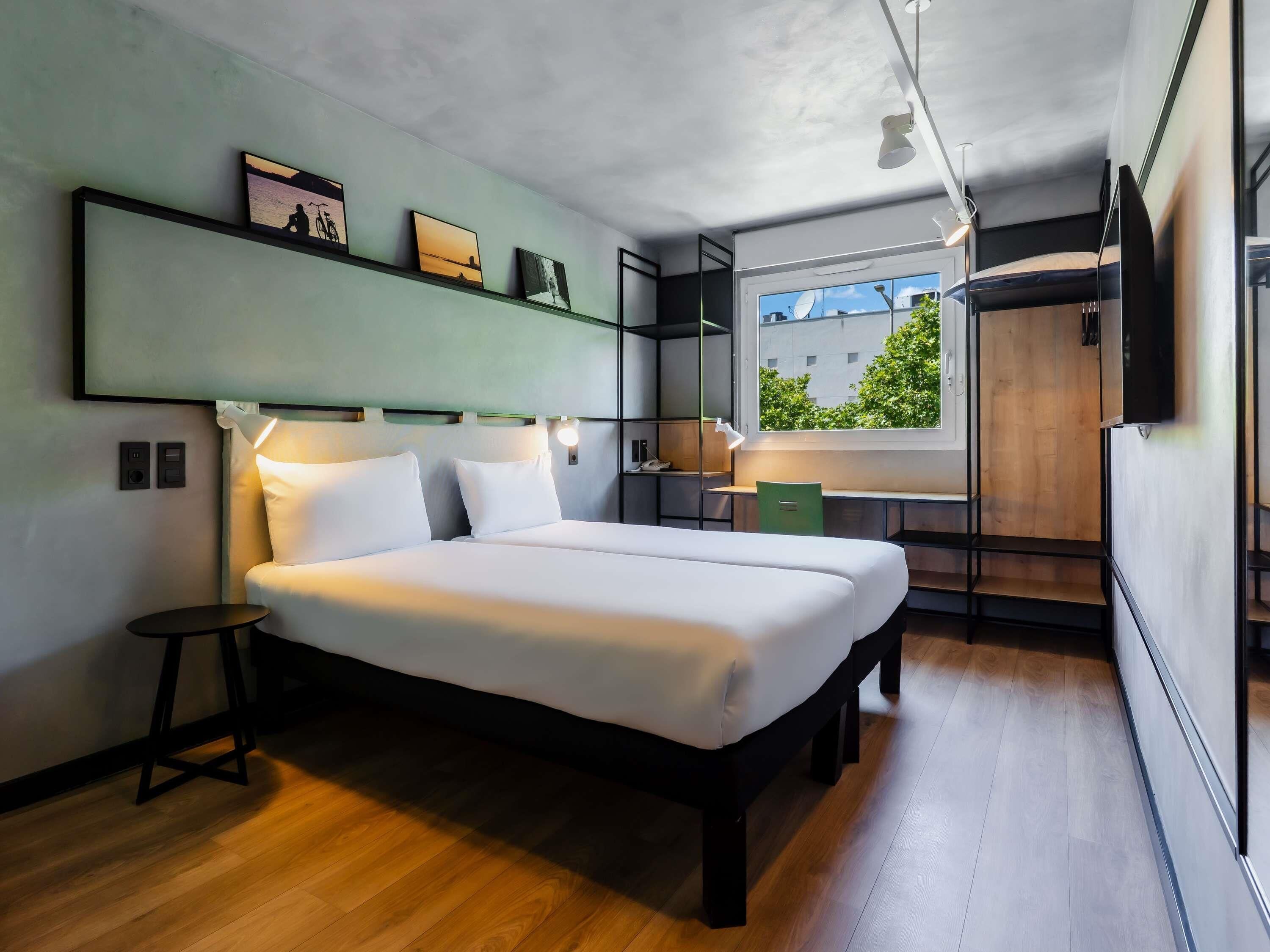 Ein modernes Hotelzimmer mit Bett, Nachttischen, Schreibtisch und Fenster mit Aussicht.