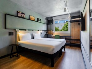 A modern hotel room with a bed, bedside tables, a desk, and a window with a view. - ibis Barcelona Castelldefels (Castelldefels)