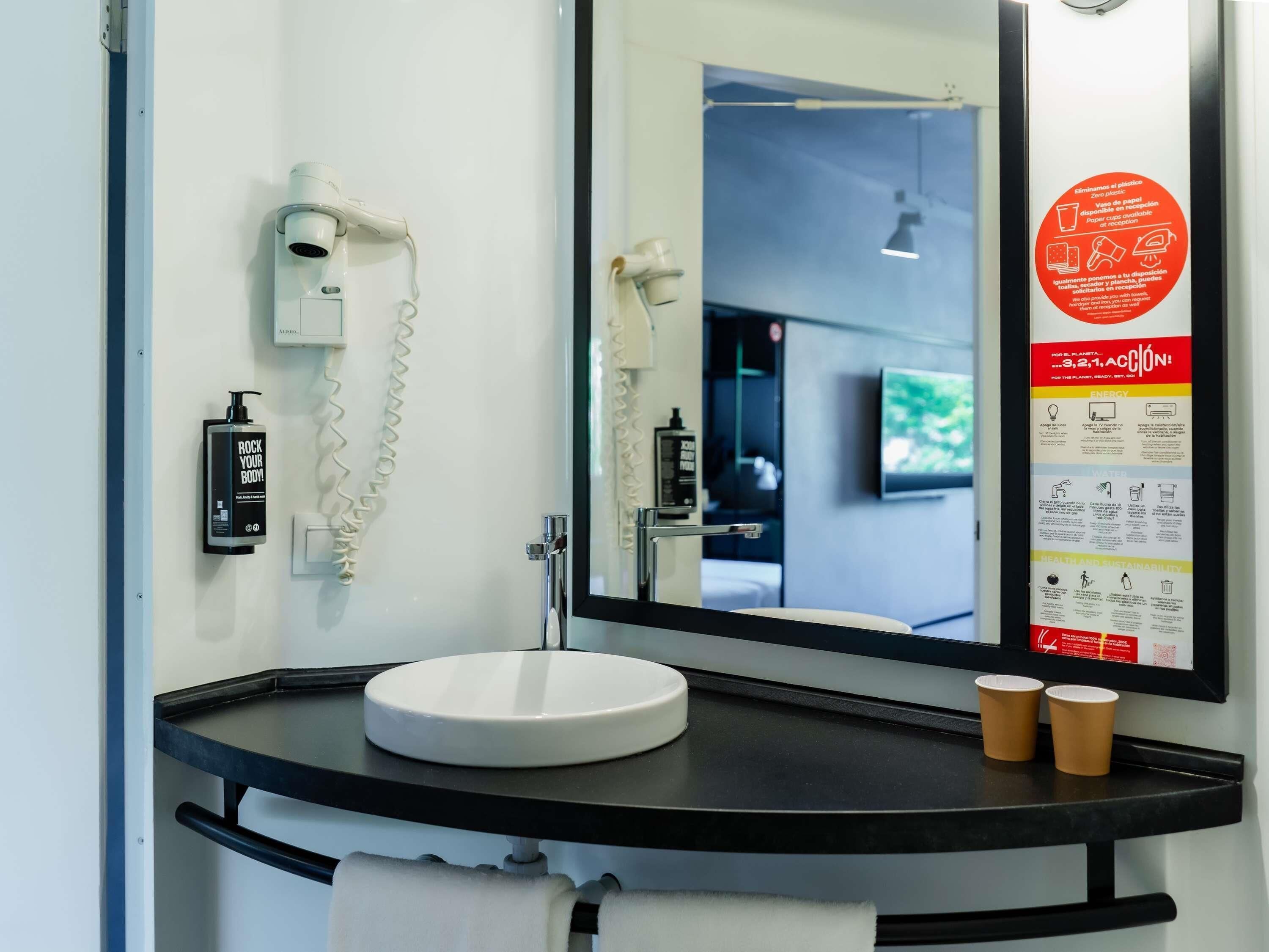 A modern bathroom with a sink, mirror, hairdryer, and a poster on the wall.