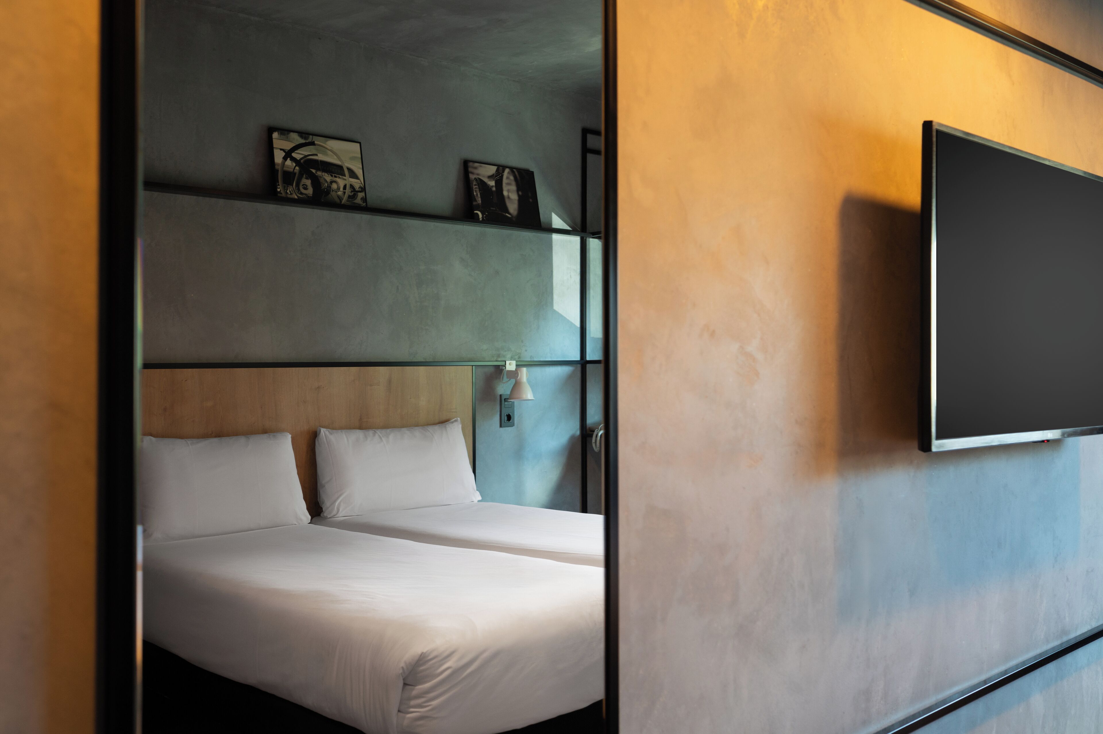 A modern hotel room with a large bed, a flat-screen TV mounted on the wall, and artwork above the bed.