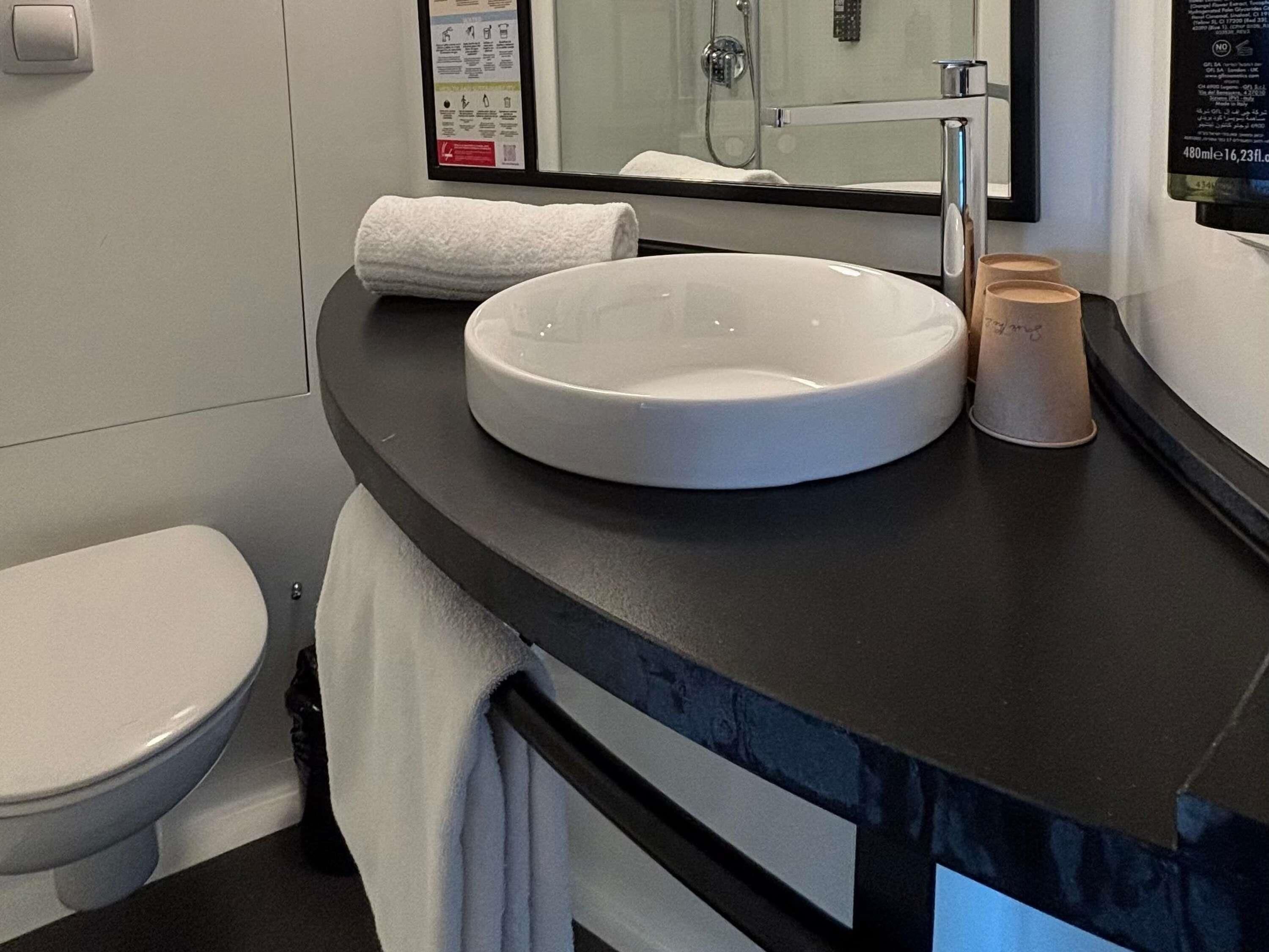 Een badkamer met een witte wastafel, toilet, handdoek en spiegel.
