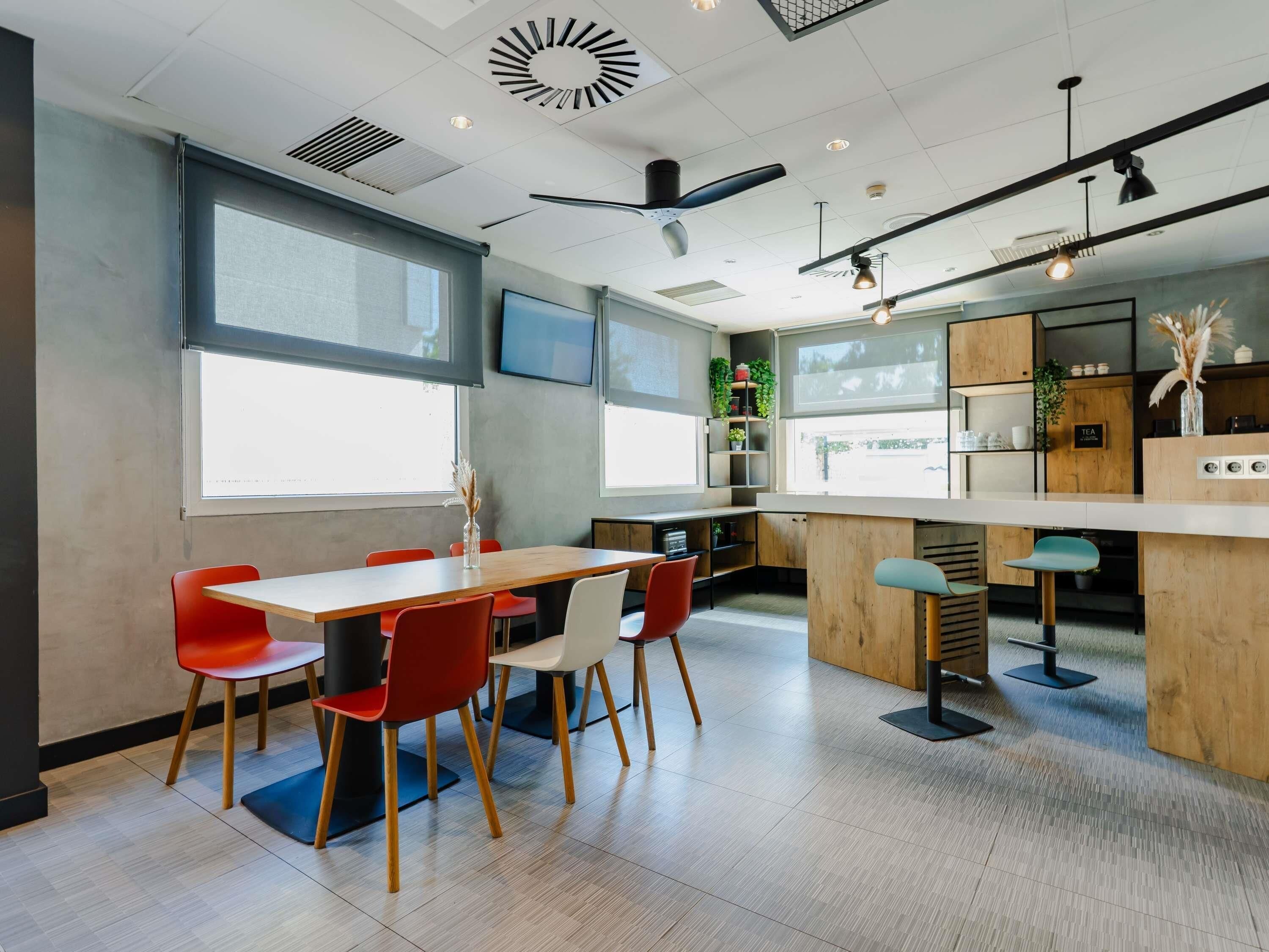 A modern kitchen with wooden cabinets, a bar area, and a dining space with red chairs.