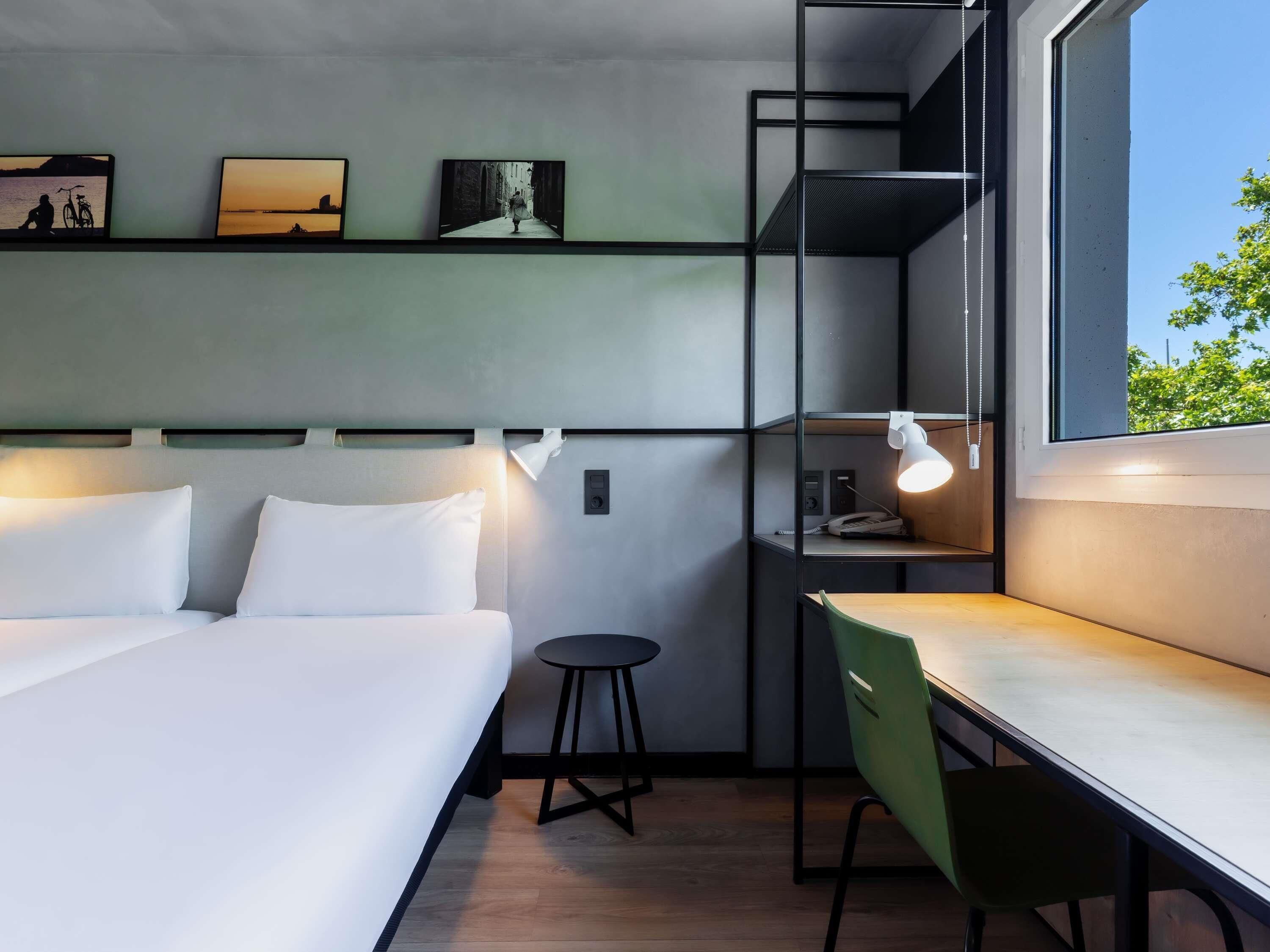 A modern hotel room with a bed, desk, and shelves with pictures.