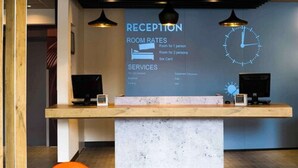 Un mostrador de recepción con pantalla digital que muestra tarifas y servicios, un reloj y una lámpara de escritorio.