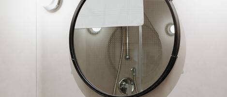 Un baño con un lavamanos verde, un espejo redondo y una toalla colgada en la pared.