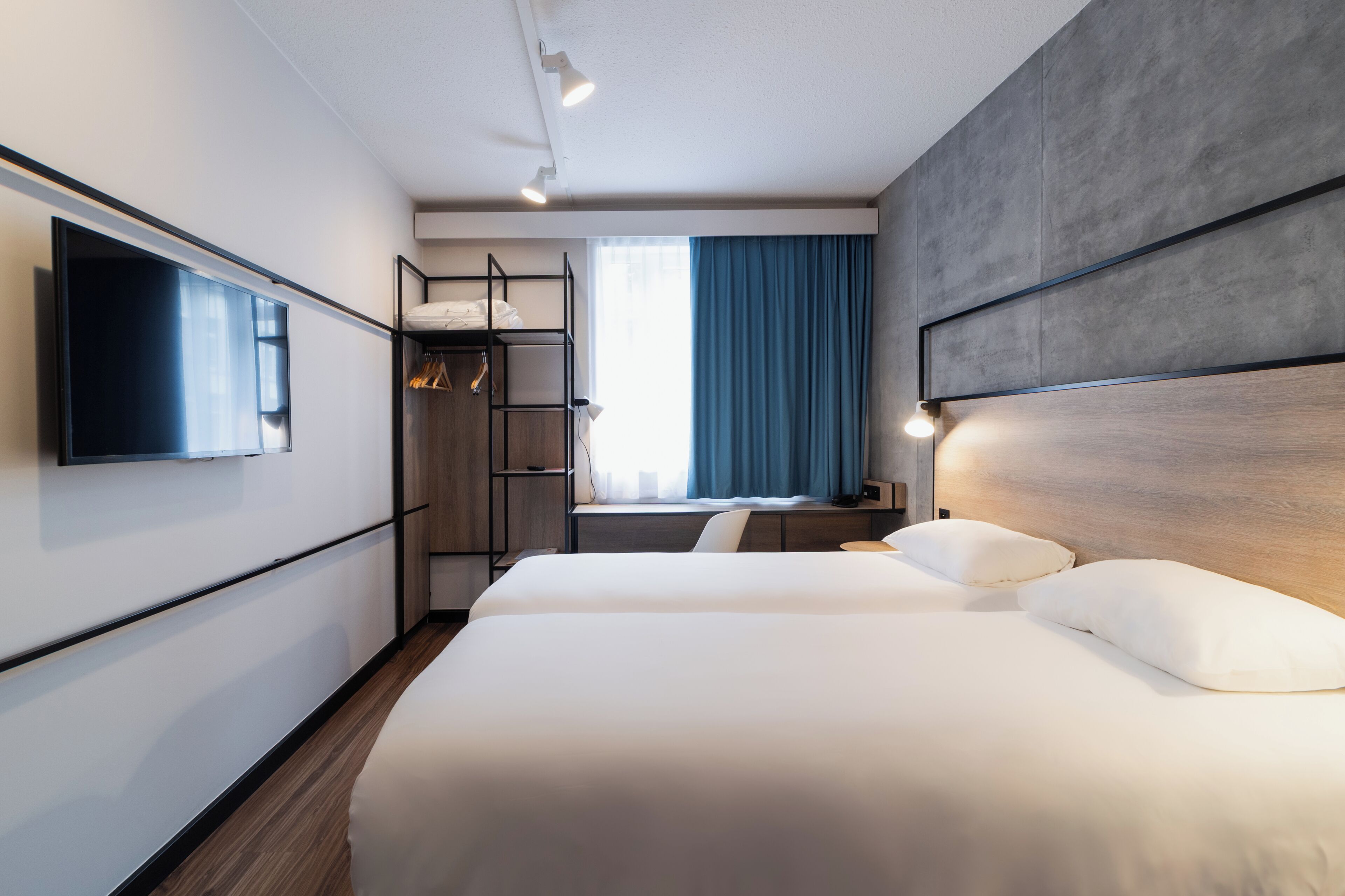 Una habitación de hotel moderna con una cama grande, un televisor montado en la pared, un armario y una ventana con cortinas.