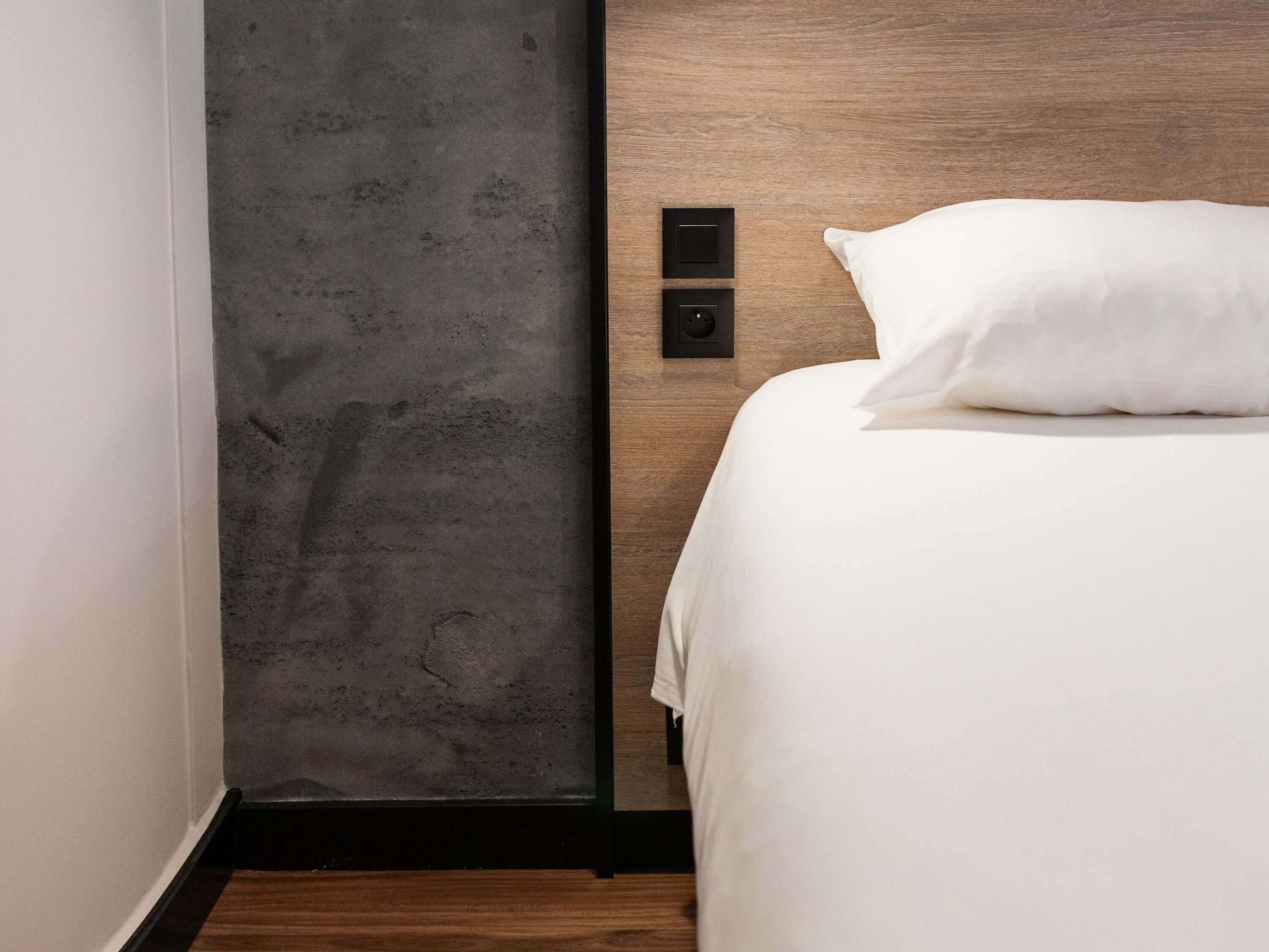 Habitación de hotel con cama, cabecera de madera, pared con textura y un enchufe.